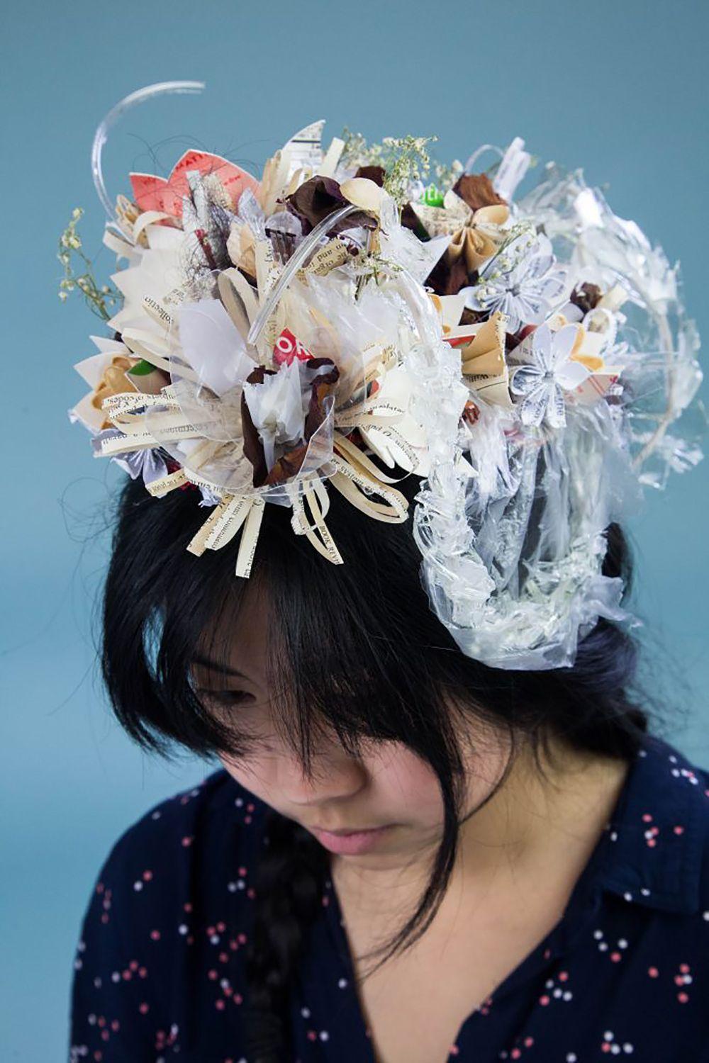 A woman with dark hair wearing a hat that appears to be made of trash and plastic.