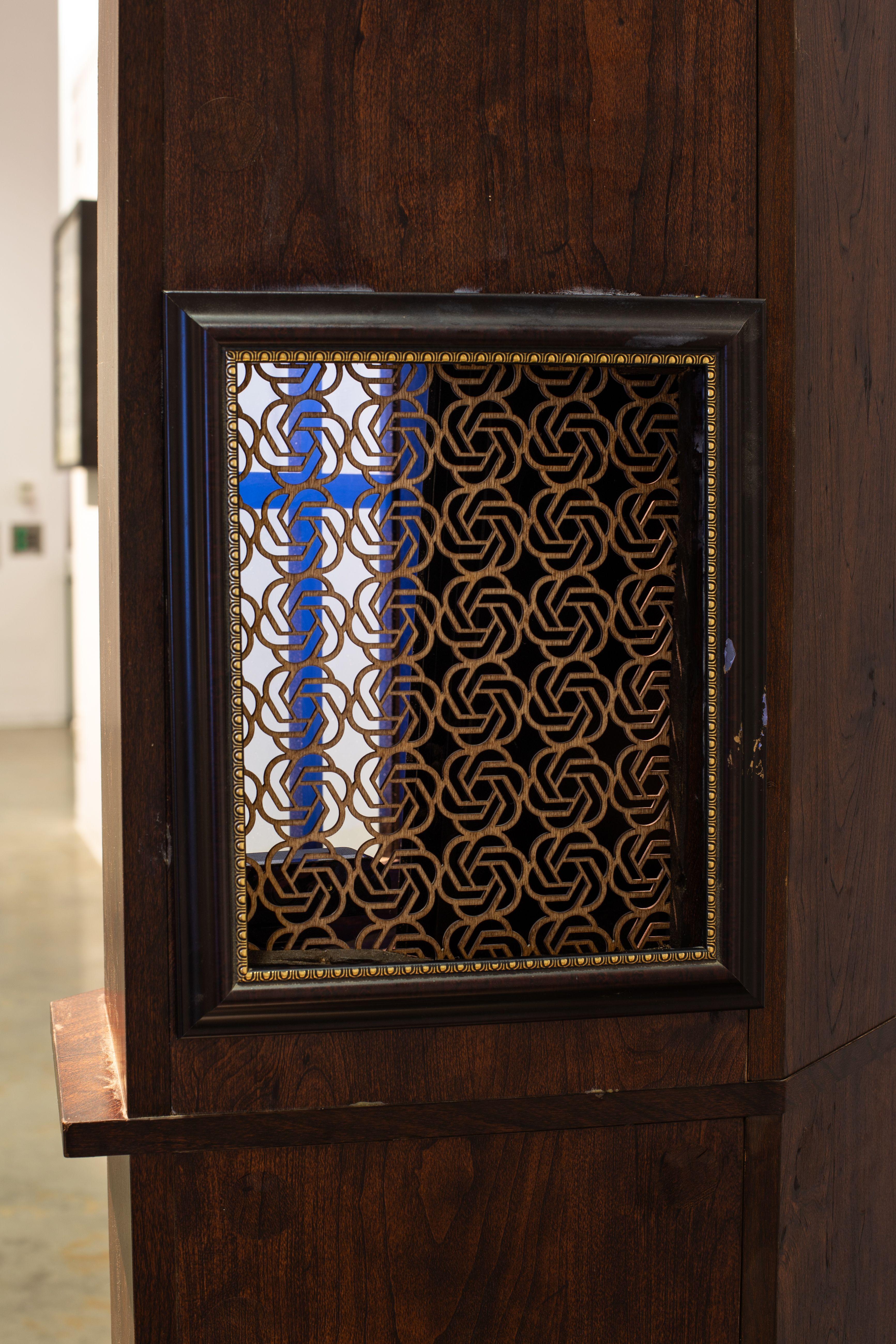 An ornimental grate on the back side of the cabinet made of a grid of ChatGPT logos, enclosed by a picture frame.  