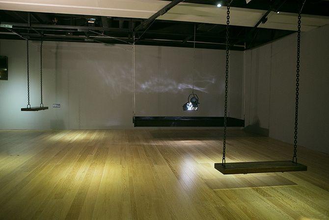 There are two swings and a stage light facing downward and a strip of black material. There is one swing on the far left back and one swing closer to the camera on the right. In the far right corner is the stage light.