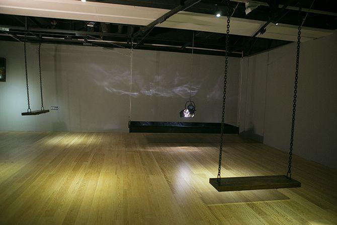 There are two swings and a stage light facing downward and a strip of black material. There is one swing on the far left back and one swing closer to the camera on the right. In the far right corner is the stage light.