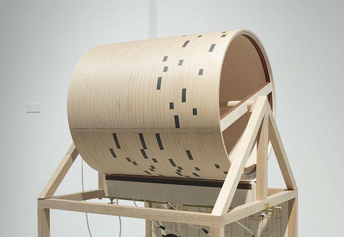 This is a close up of the cylinder on top of the light beige machine. It seems to have small black rectangles on it in a particular pattern, likely so that the machine can read the rectangles, which are arranged in lines, and interpret music of some kind.