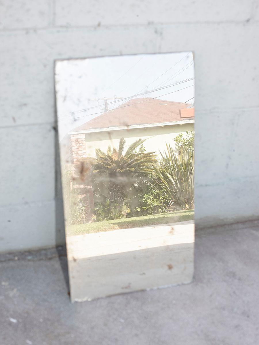 A mirror leaning against a wall outside reflecting a house