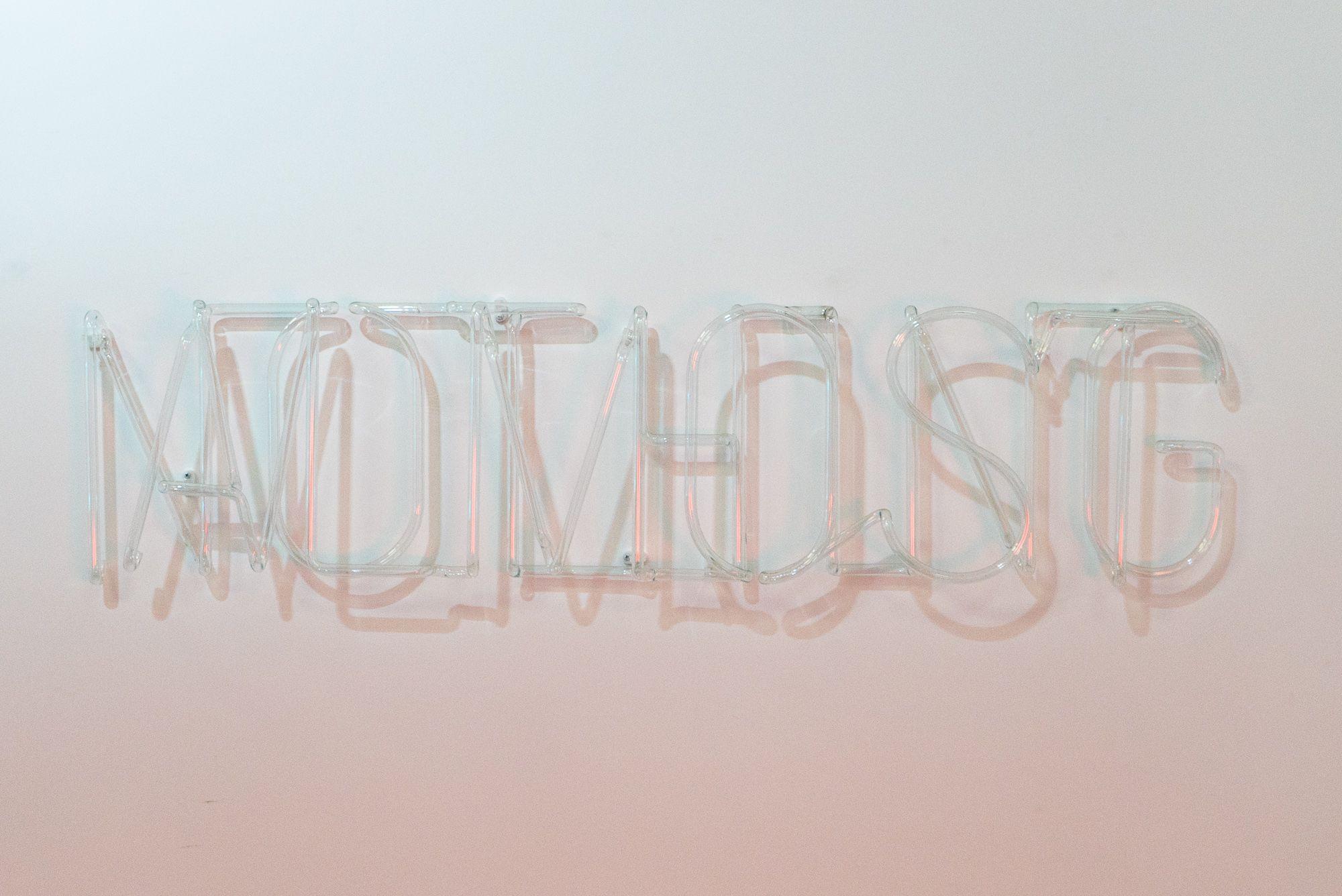 The words "ALMOST NOTHING" are sculpted out of clear glass tubing, they are mounted on the wall overlapping.