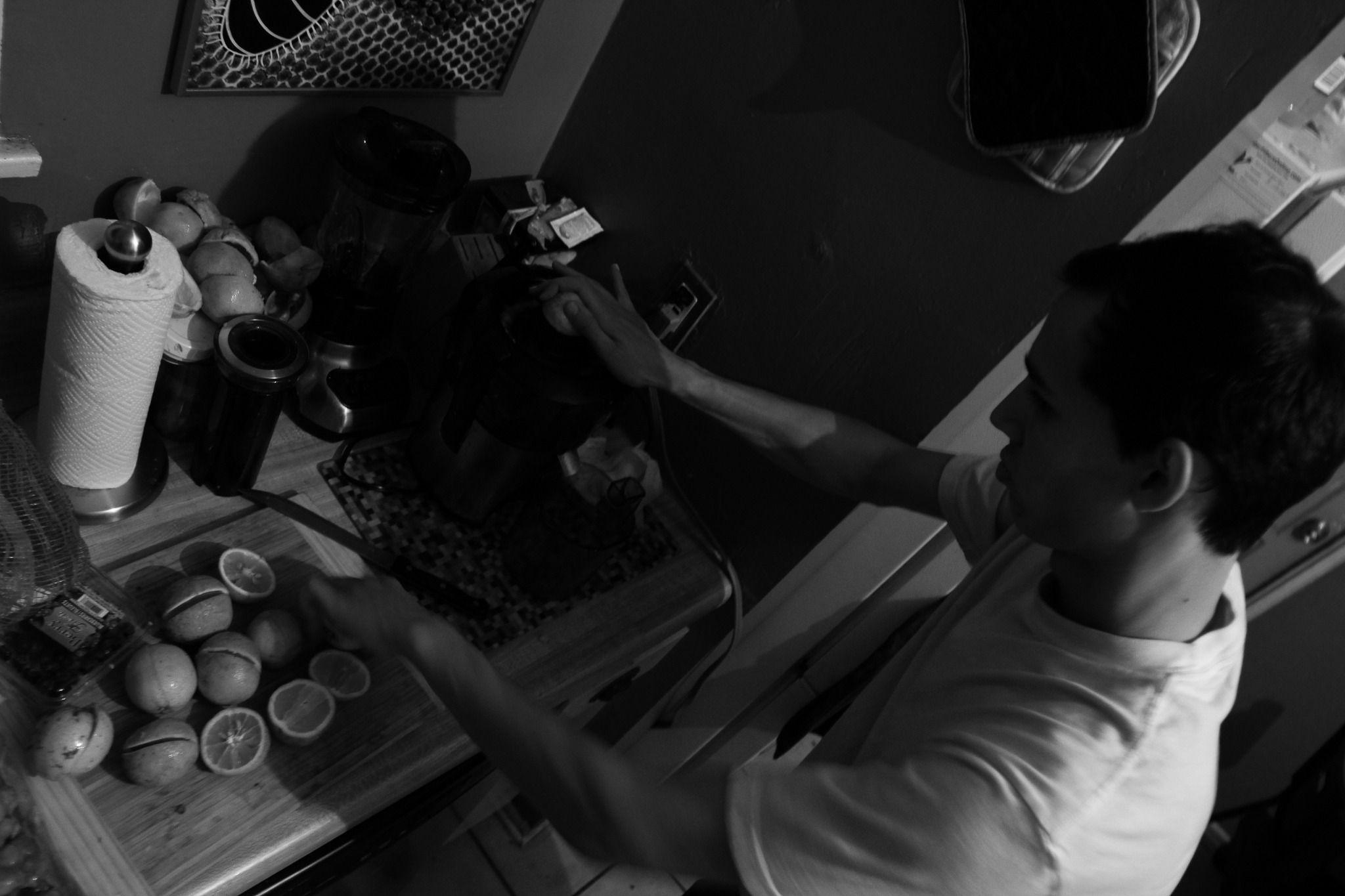 This is a dark grayscale photo taken diagonally from above of someone cutting limes in a kitchen.